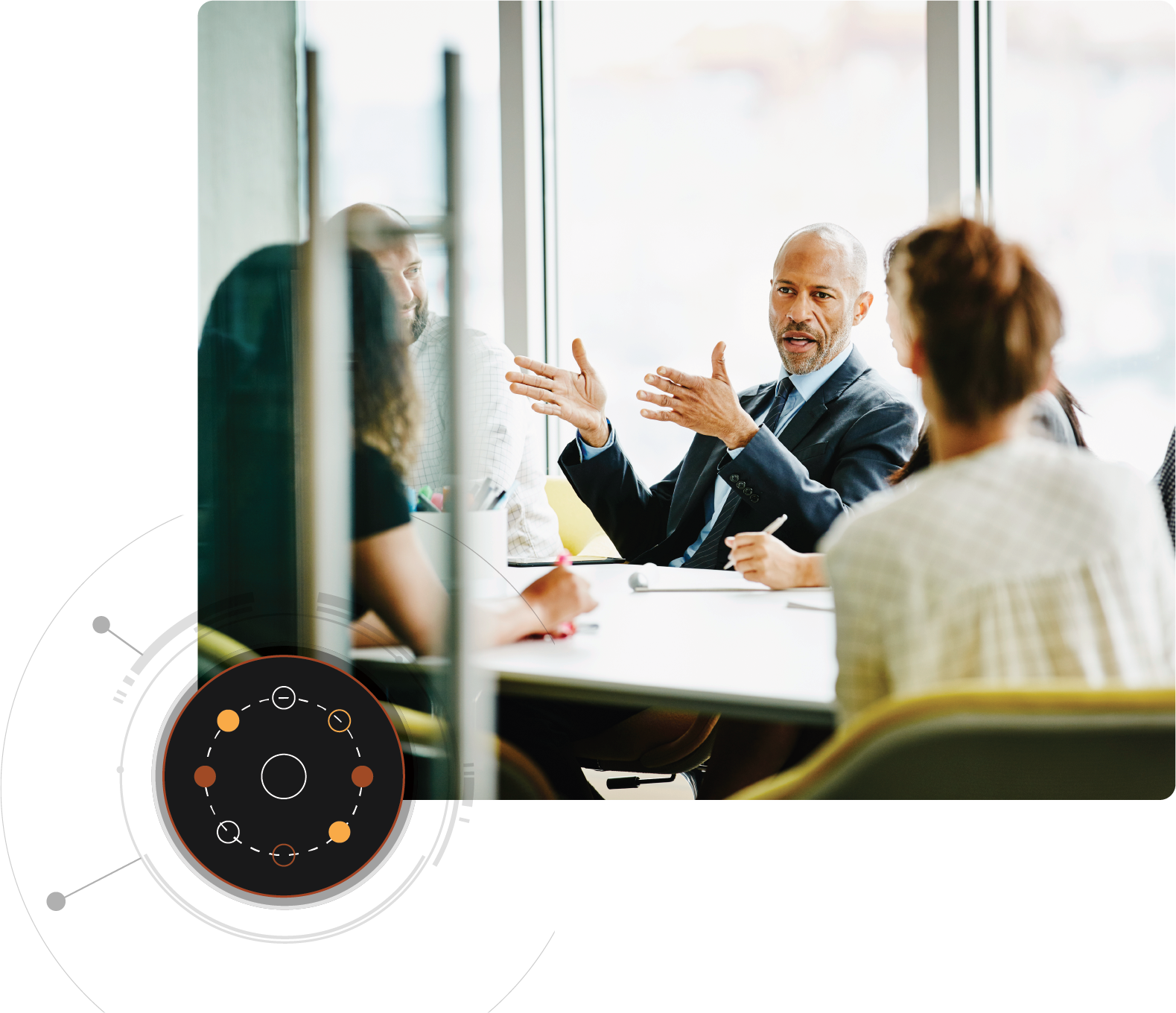 한 남성이 회의용 탁자 주변에 둘러앉은 여러 사람에게 말하고 있고 왼쪽 하단 모서리에 원형 그래픽 오버레이가 있습니다.